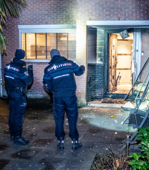 twee politieagenten schijnen met een zaklamp op een opgeblazen voordeur van een woonhuis