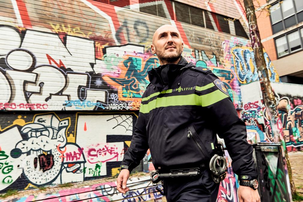 Wijkagent Tugay loopt door de wijk. Je ziet een muur met graffiti. 